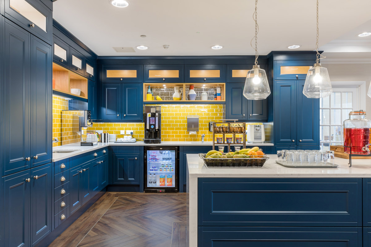 Kitchen with dark blue cabinets, bright yellow tiles and white countertops. Dark wooden floor laid in herringbone pattern with authentic aged oak hues.