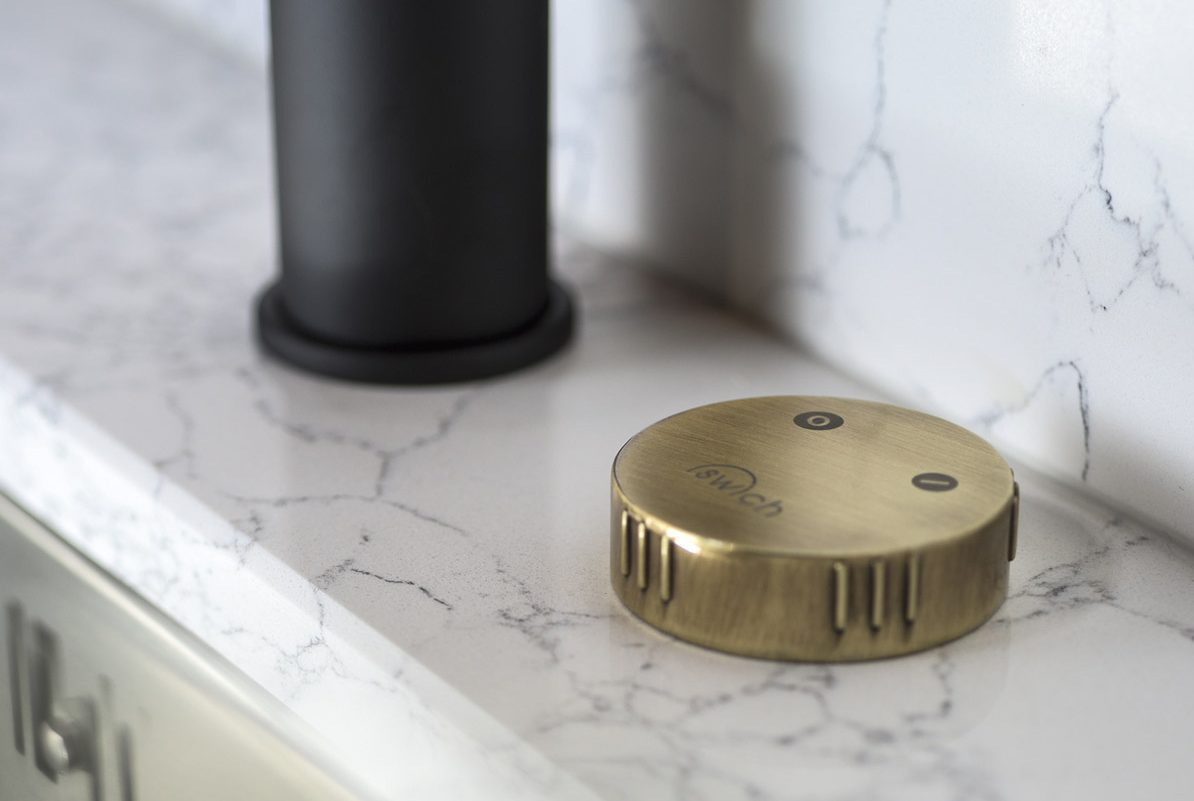 A close-up of a round bronze filter water switch on a marble kitchen surface.