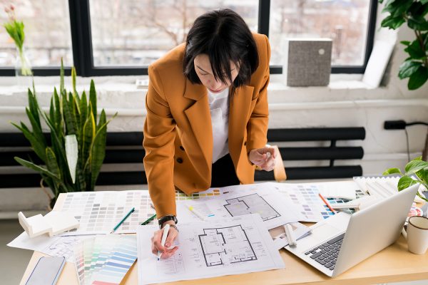 Woman architect working on interior renovation in workplace. Designer choosing color samples according to the visualization and blueprints of the project. Architecture and interior design concept.